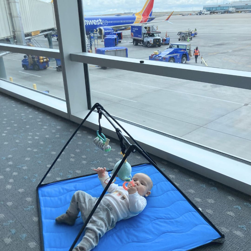 Baby playing on the Lay & Play Adventure Mat, a portable travel baby play mat, at an airport gate.